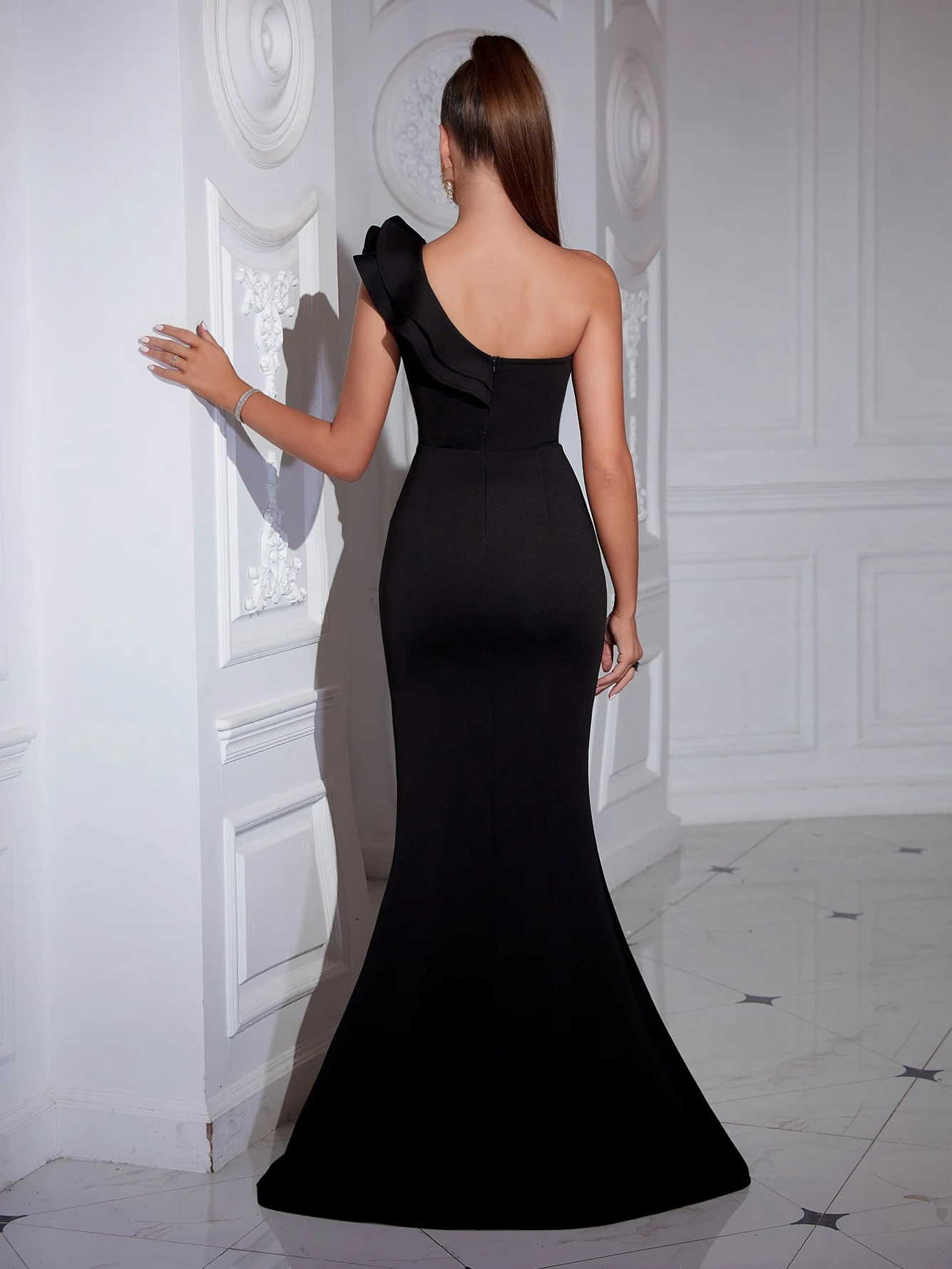 Woman with her back turned wearing a black one-shoulder evening gown showing her back.