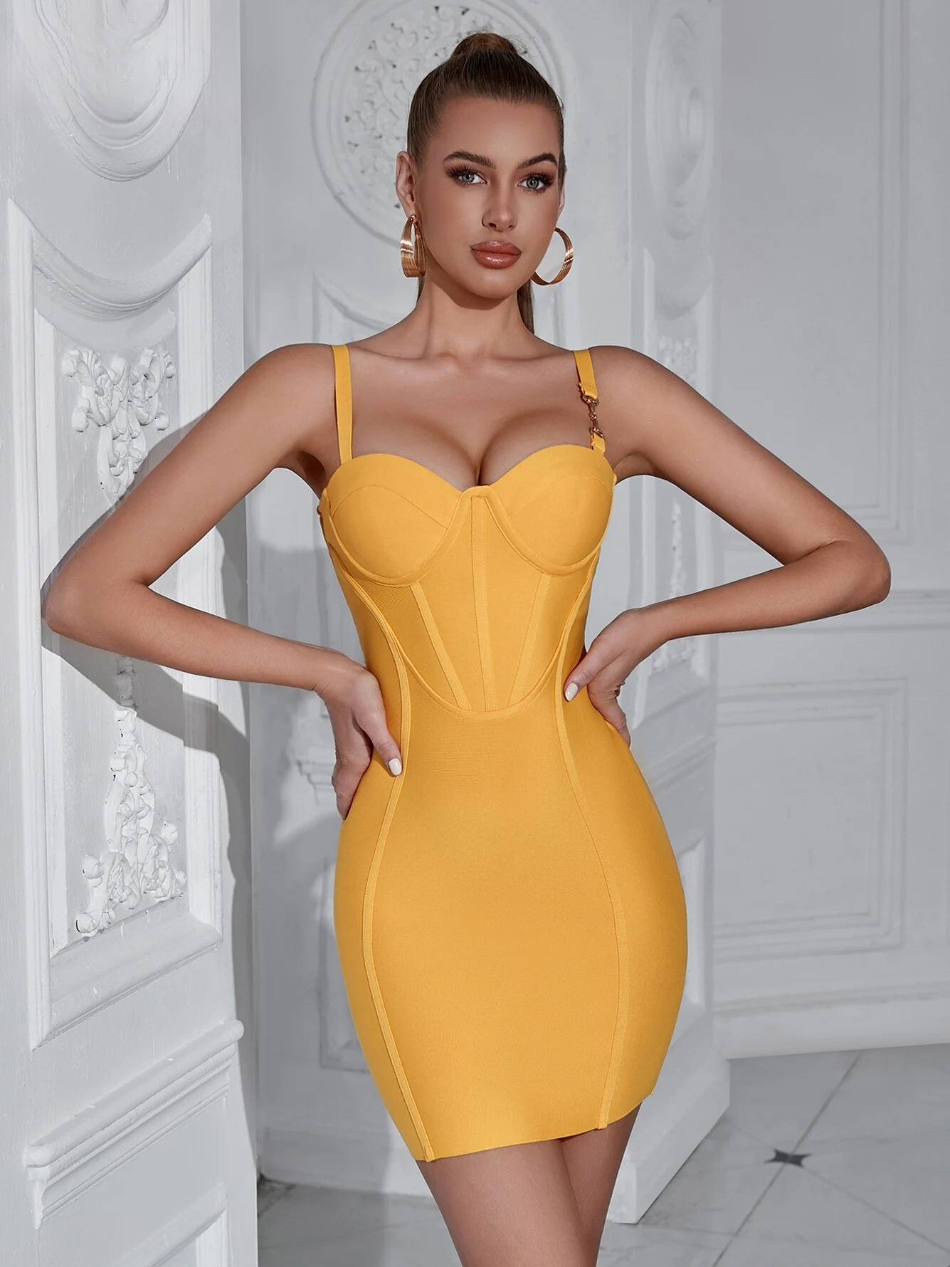 A woman wearing a yellow strapless bodycon dress and gold hoop earings with her hands on her waist.